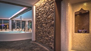 A modern indoor pool area with stone walls and a tiled wall with a decorative alcove.