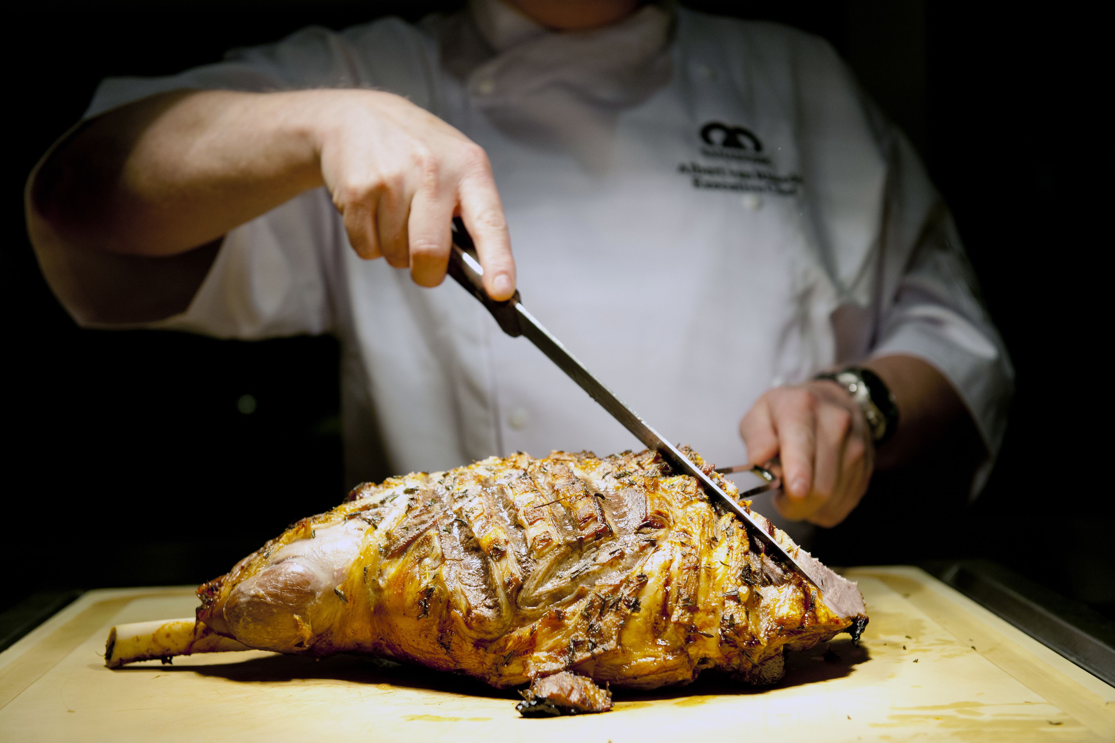 Um chef fatiando uma grande carne assada em uma tábua de corte.