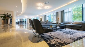 A spacious lobby with a modern design, featuring a black leather chair, a round coffee table, and a large window offering a view of greenery.