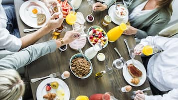 Um grupo de pessoas almoçando à mesa de madeira, com diversas opções de café da manhã e bebidas.