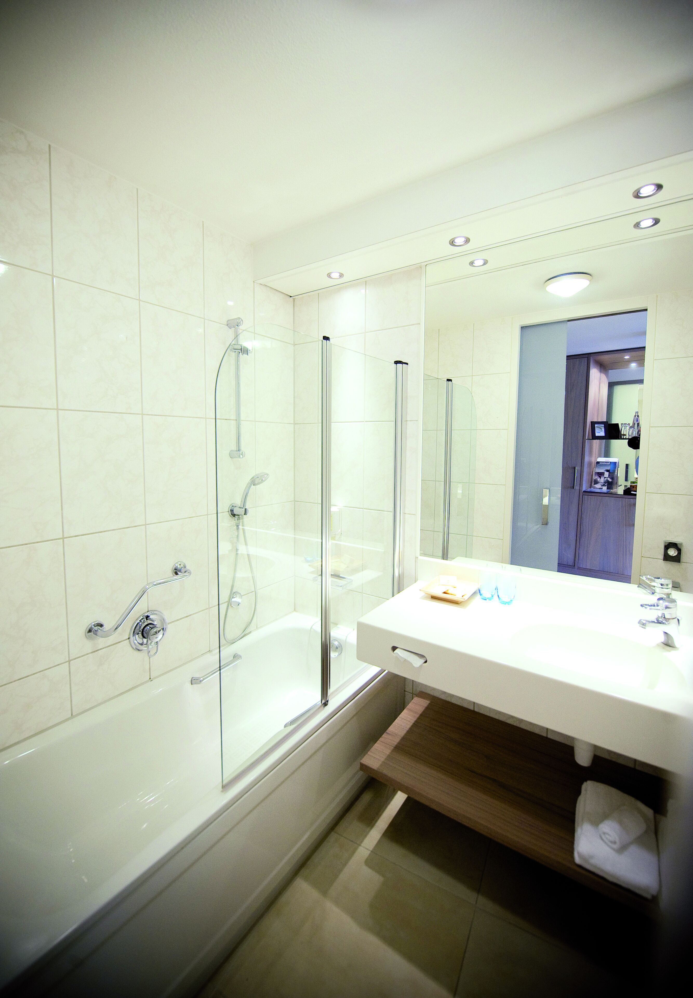 Un baño moderno con ducha de vidrio, un lavamanos blanco con espejo y un mueble de tocador de madera.
