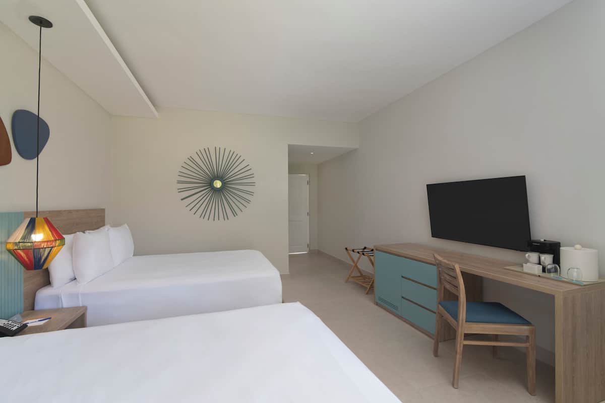 Habitación de hotel con dos camas, un escritorio con silla, televisor y un adorno en la pared.