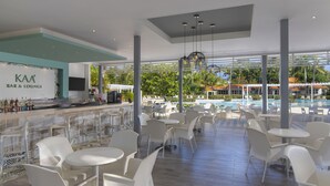 Een moderne bar en lounge met witte stoelen en tafels, een bar met een bord en uitzicht op een zwembad en groen.