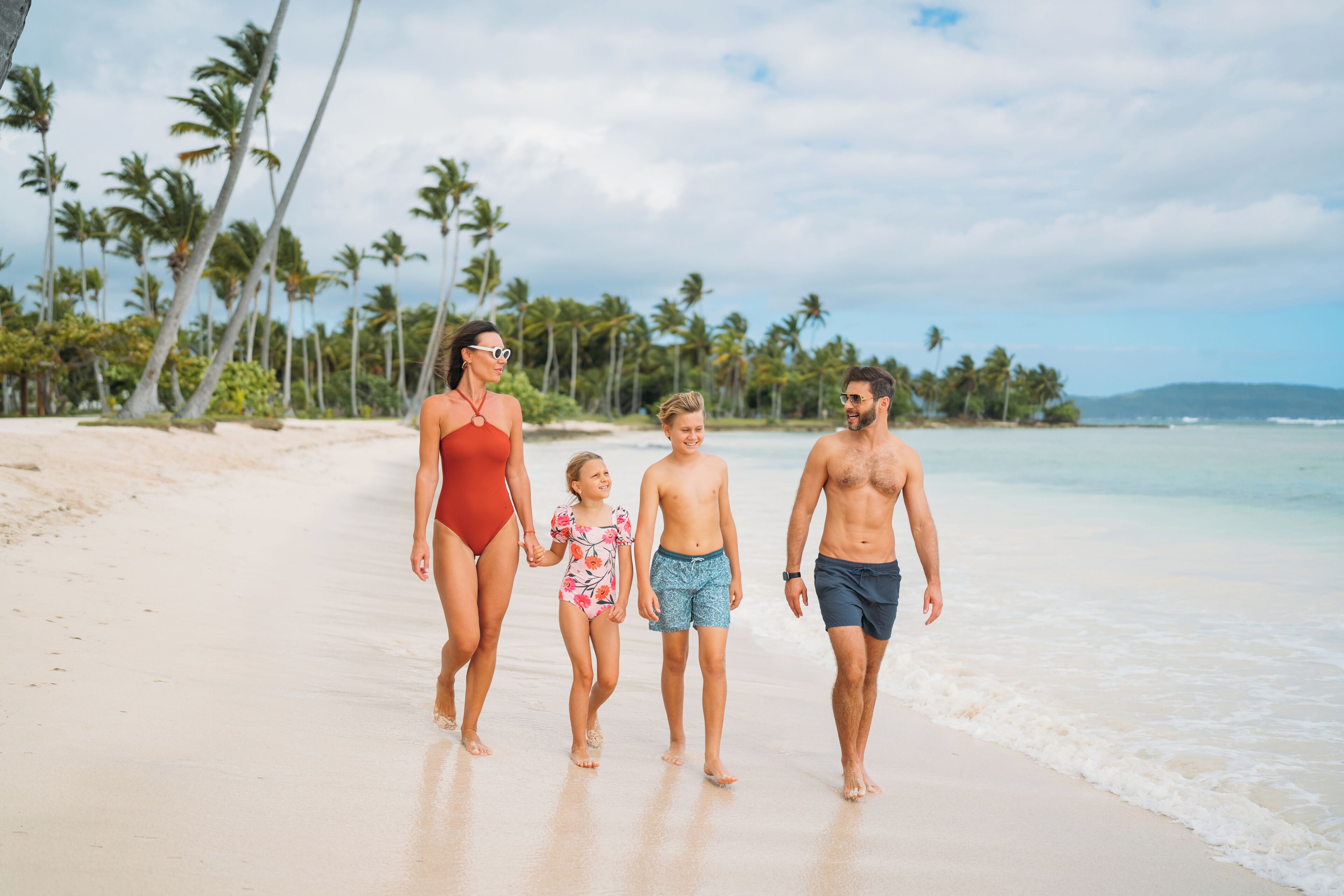 A family walking on a beach with palm trees and ocean in the background.