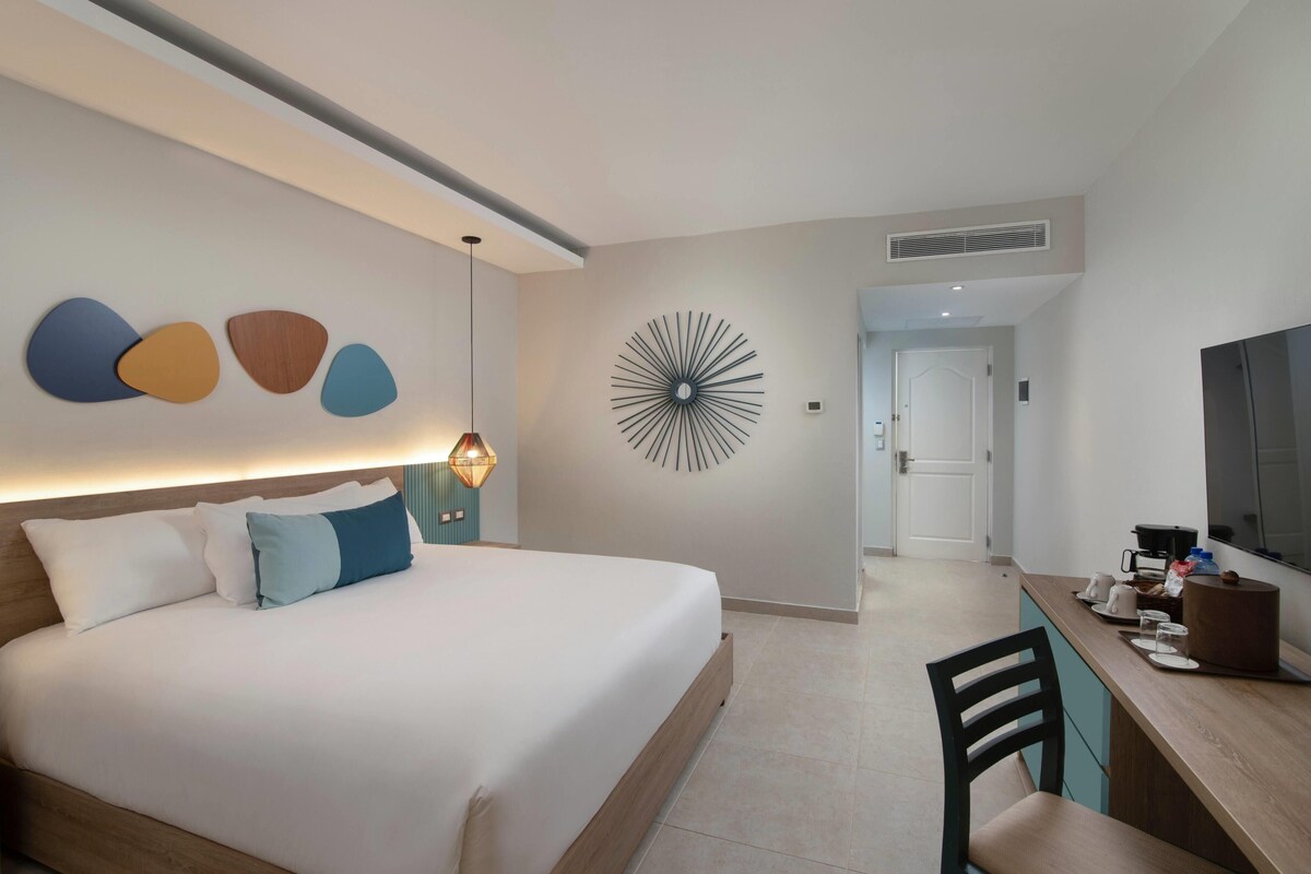 Ein Hotelzimmer mit Bett, Schreibtisch, Stuhl, Fernseher und einer Wand mit einem runden Dekor.