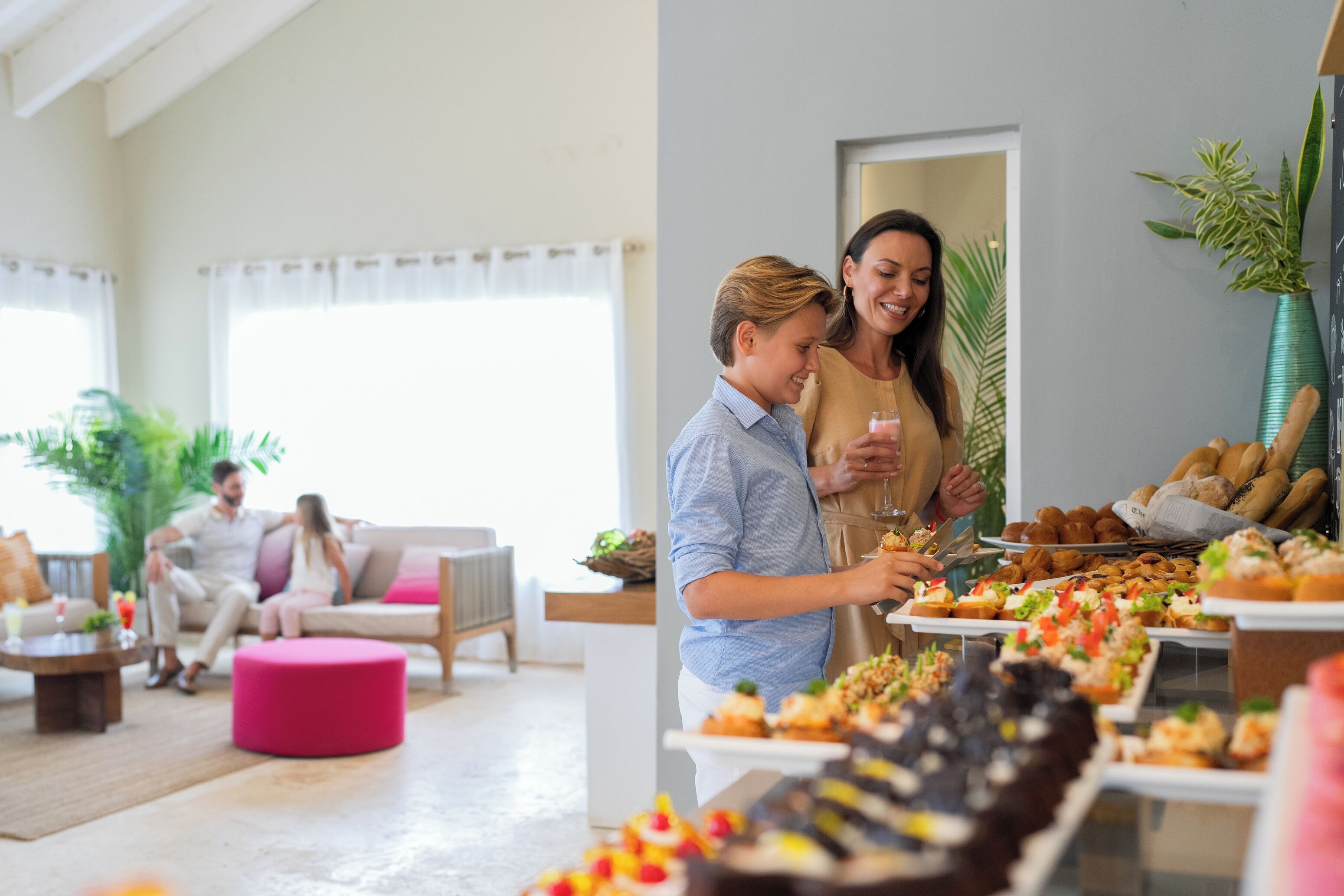 Un vaste espace de vie doté d’un intérieur moderne, une table à manger où sont présentés divers plats, et un coin salon confortable agrémenté d’un pouf rose.