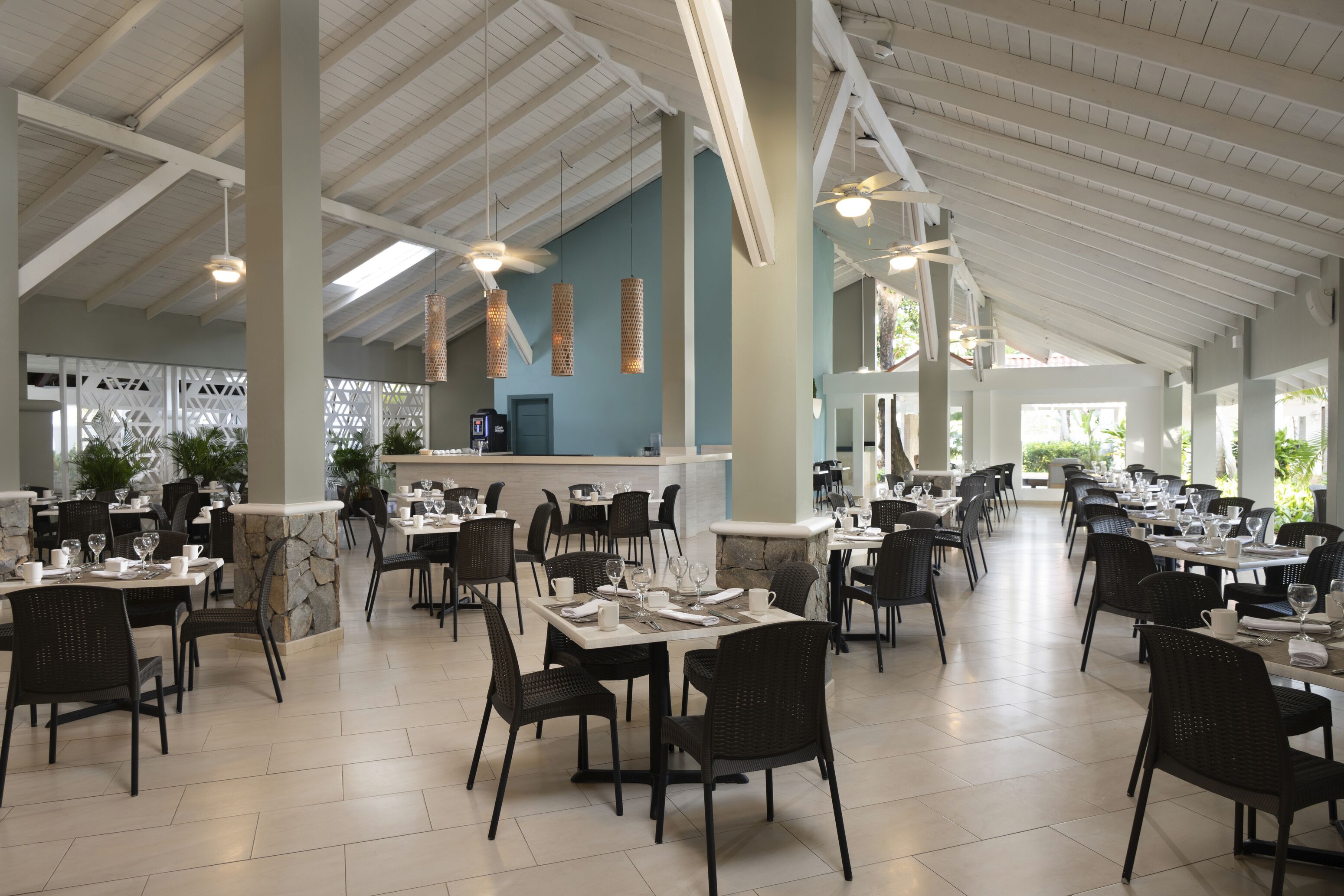 Un comedor amplio con techos altos, varias mesas y sillas, y una barra central.