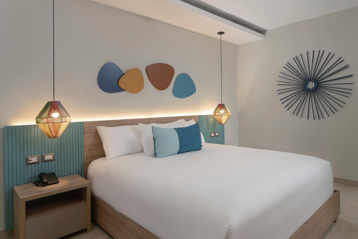 Ein modernes Hotelzimmer mit einem großen Bett, zwei Nachttischen, einem Wandtelefon und zwei Pendelleuchten.