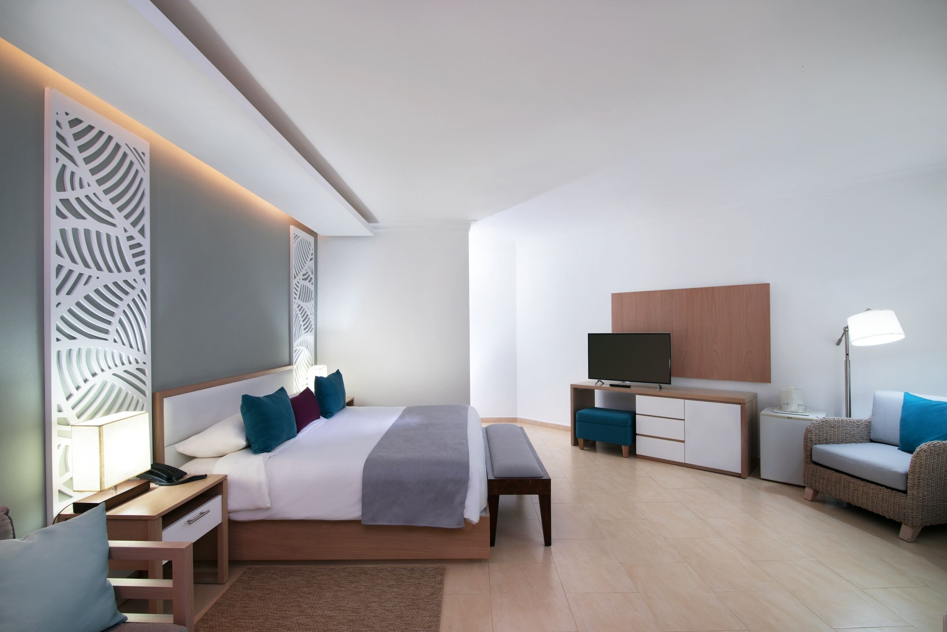 A modern hotel room with a large bed, bedside tables, a TV, a desk, and a seating area.