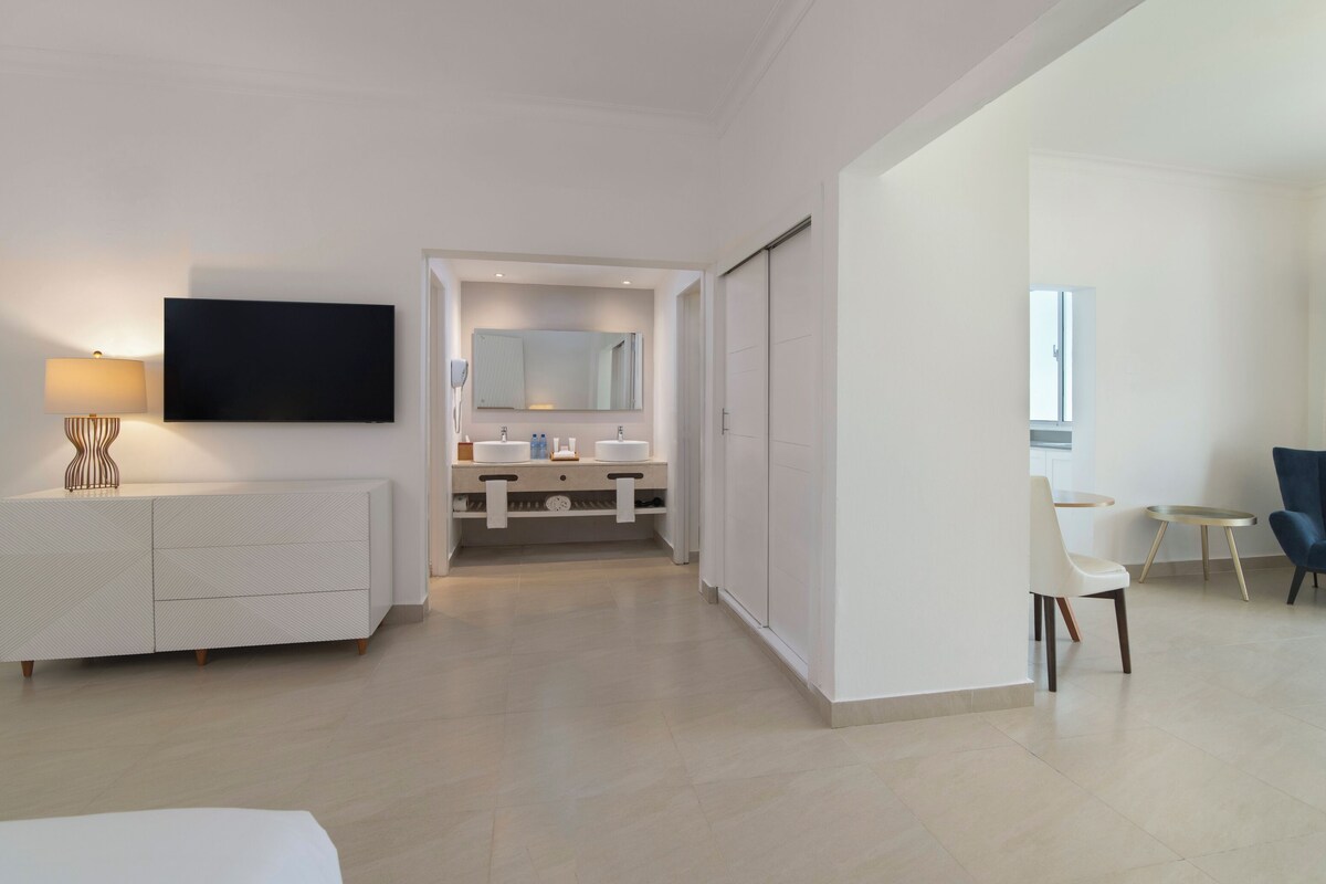 Ein modernes Hotelzimmer mit Fernseher, Schminktisch mit Spiegel, Sofa und Sessel.