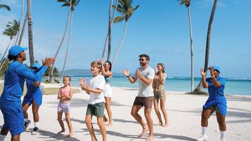 Un grupo de personas realizando una danza sincronizada en una playa con palmeras y el océano al fondo.