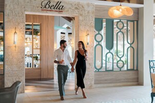 Una pareja caminando por un interior moderno, con el restaurante 'Bella Ristorante Italiano' al fondo.