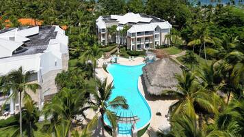 Relax by the resort's pool surrounded by lush greenery and palm trees, with a view of the ocean and distant islands.