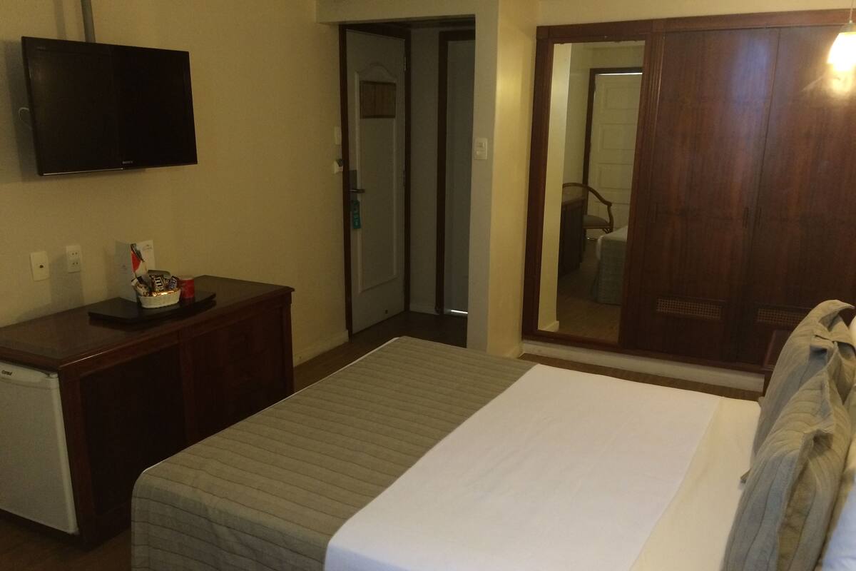 A hotel room with a bed, a small desk with a television, and a wardrobe.