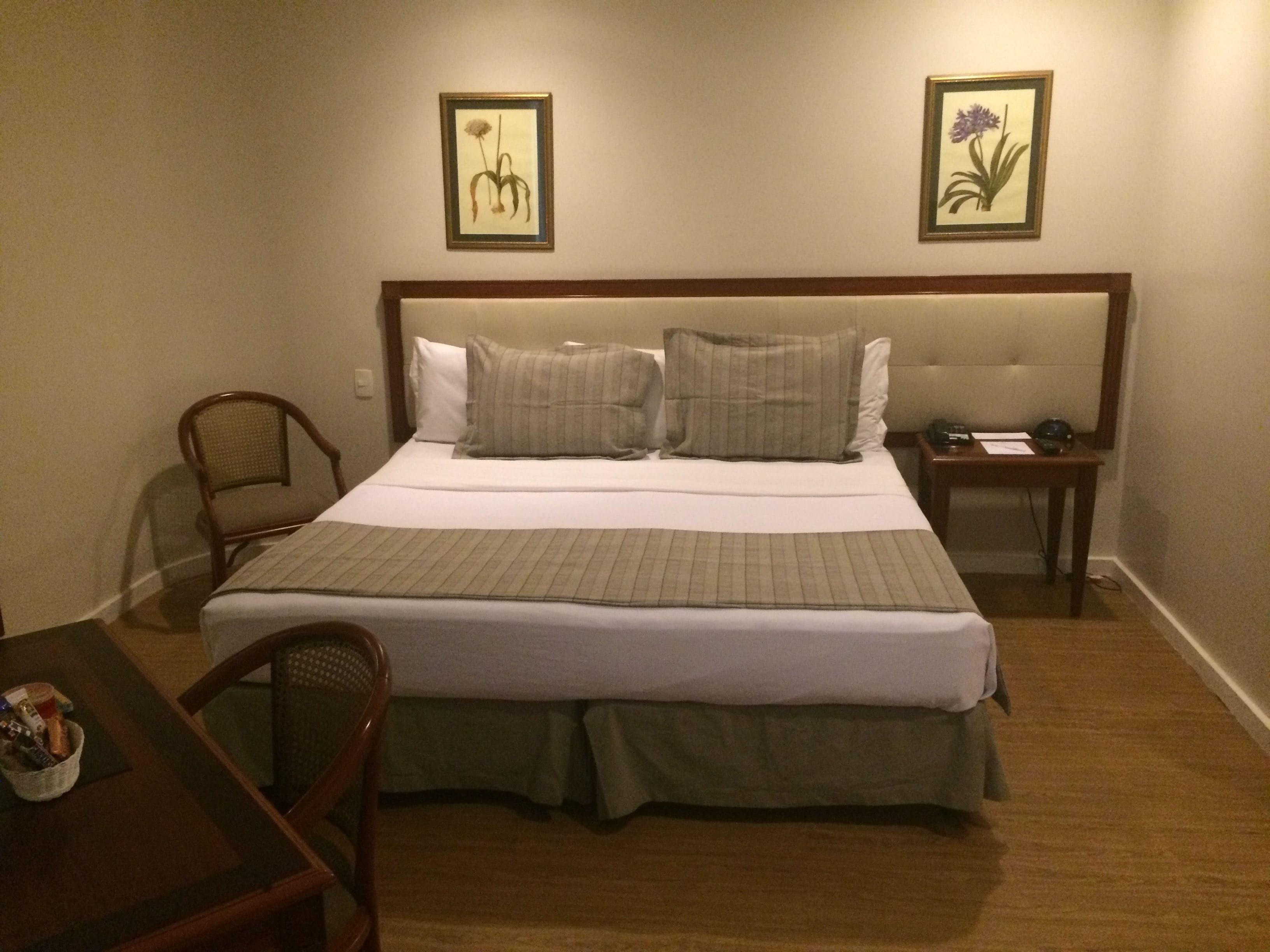 A neatly made bed with a green bedspread, two pillows, a wooden nightstand with a lamp, and a chair.