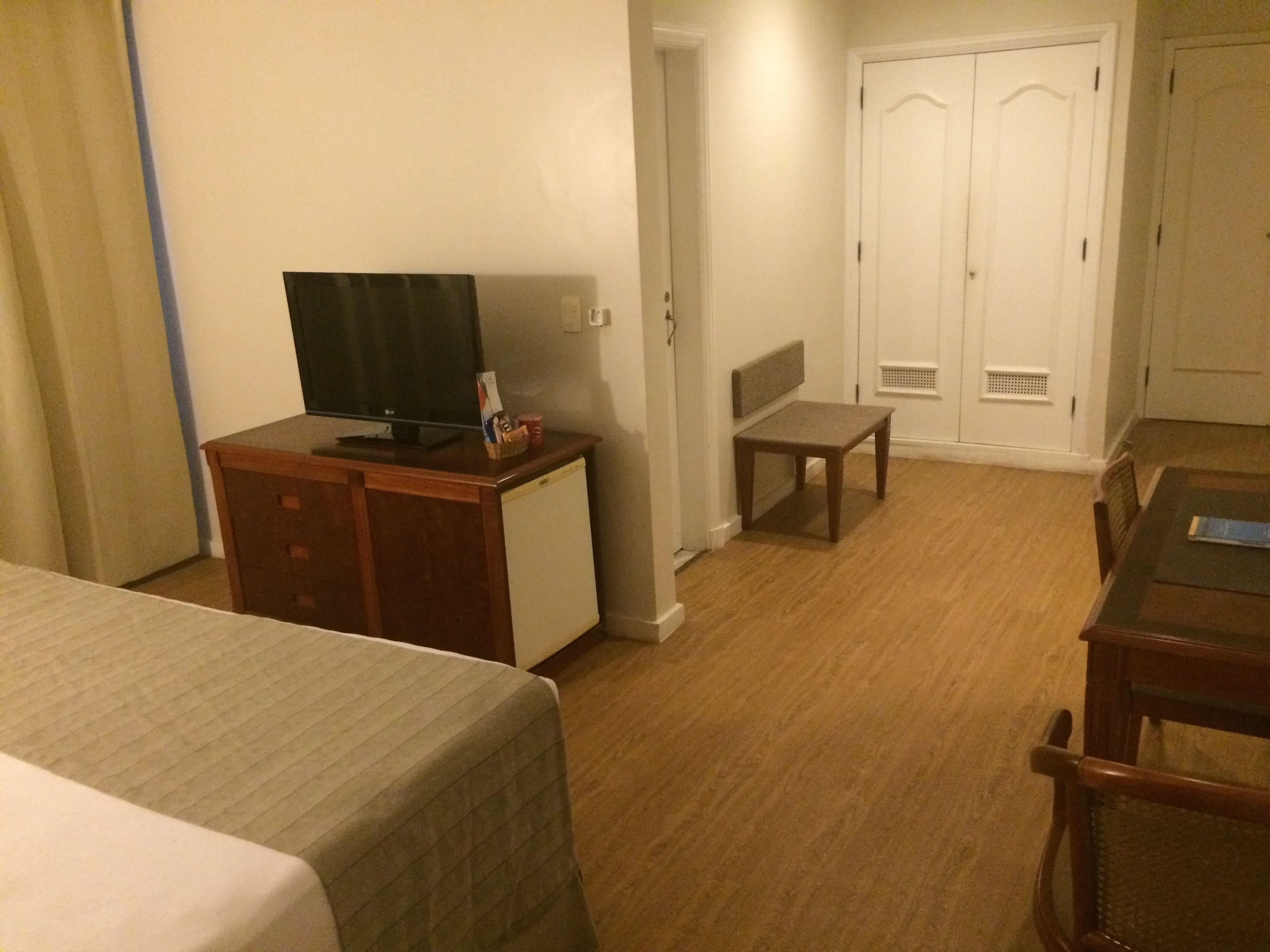 A hotel room with a bed, a desk with a television, a small table, and a wardrobe.