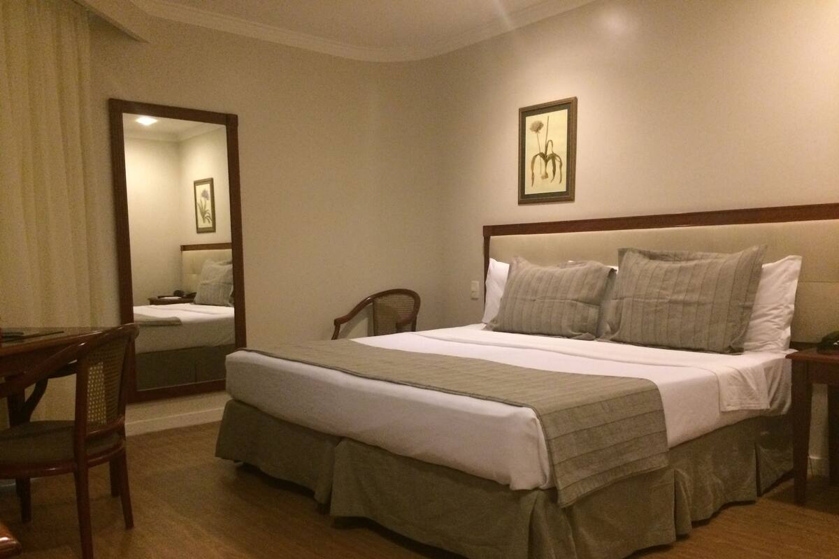 A hotel room with a bed, a chair, a desk, and a mirror.
