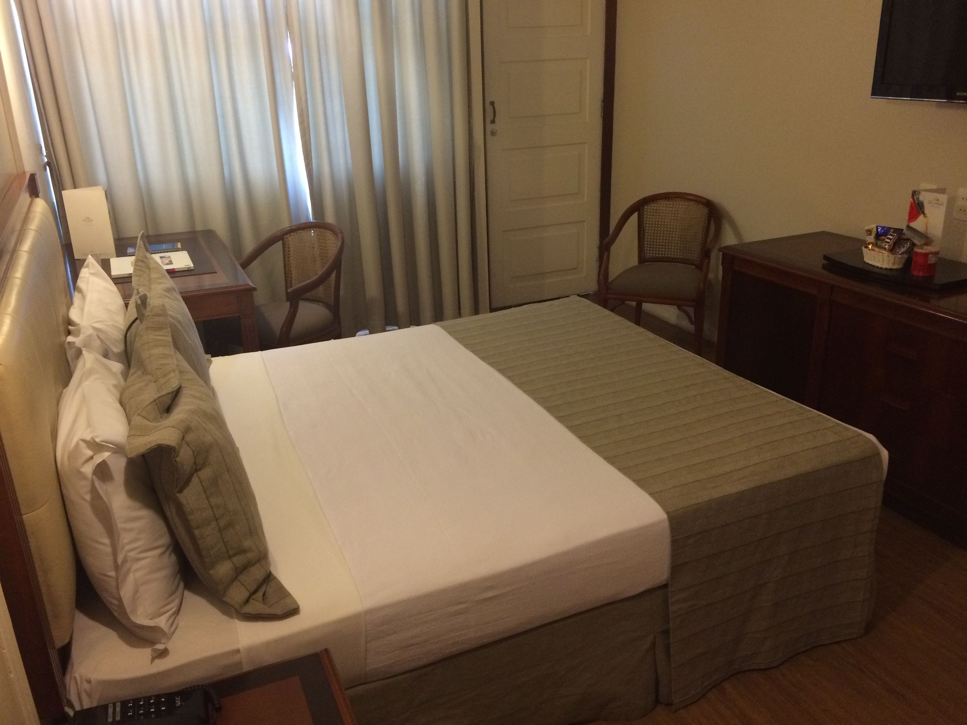 Une chambre d’hôtel avec un lit, deux chaises, un bureau avec une lampe et un téléviseur fixé au mur.