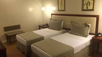 A hotel room with two single beds, a bench, a bedside table with a lamp, and a framed picture on the wall.
