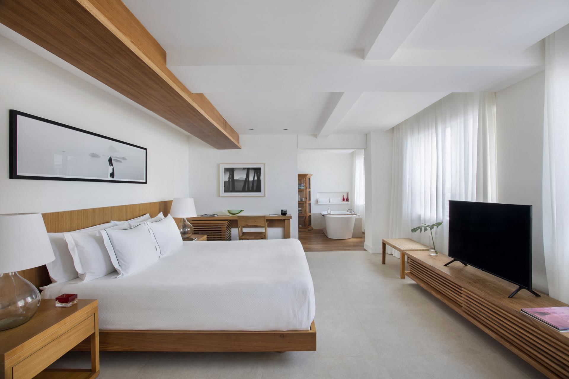 A modern hotel room with a large bed, a TV, a wooden headboard, and a view of the bathroom.