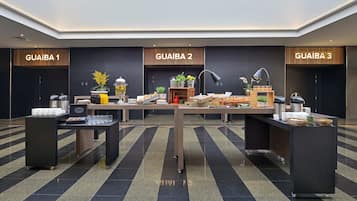 Um lobby de hotel moderno com três balcões de atendimento identificados como GUAIBA 1, GUAIBA 2 e GUAIBA 3. Cada balcão possui uma máquina de café, seleção de bebidas e diversos petiscos. O chão apresenta um padrão listrado em preto e cinza, e as paredes são escuras com detalhes em madeira.