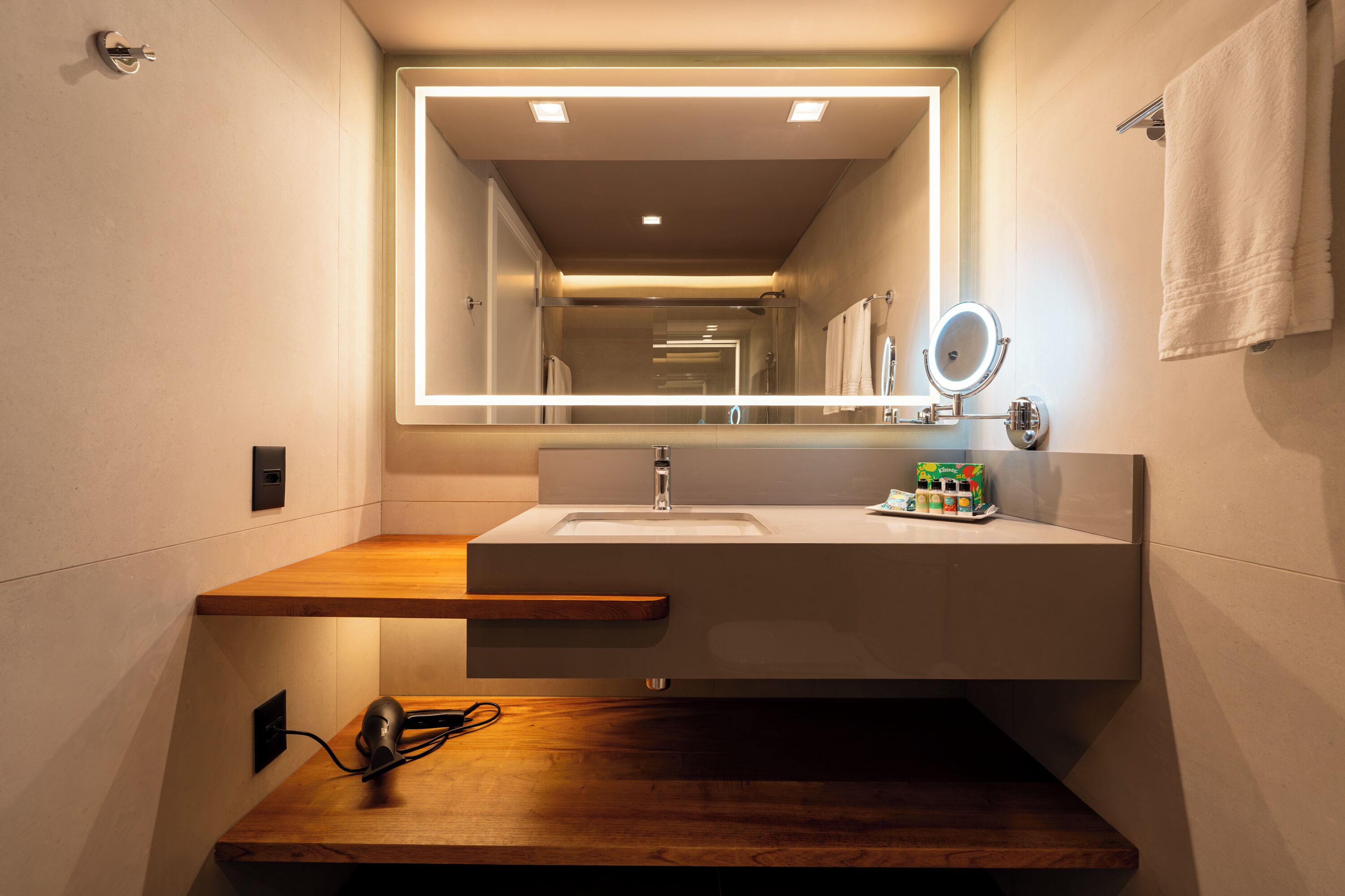 A modern bathroom with a large mirror, a sink, and a wooden countertop.