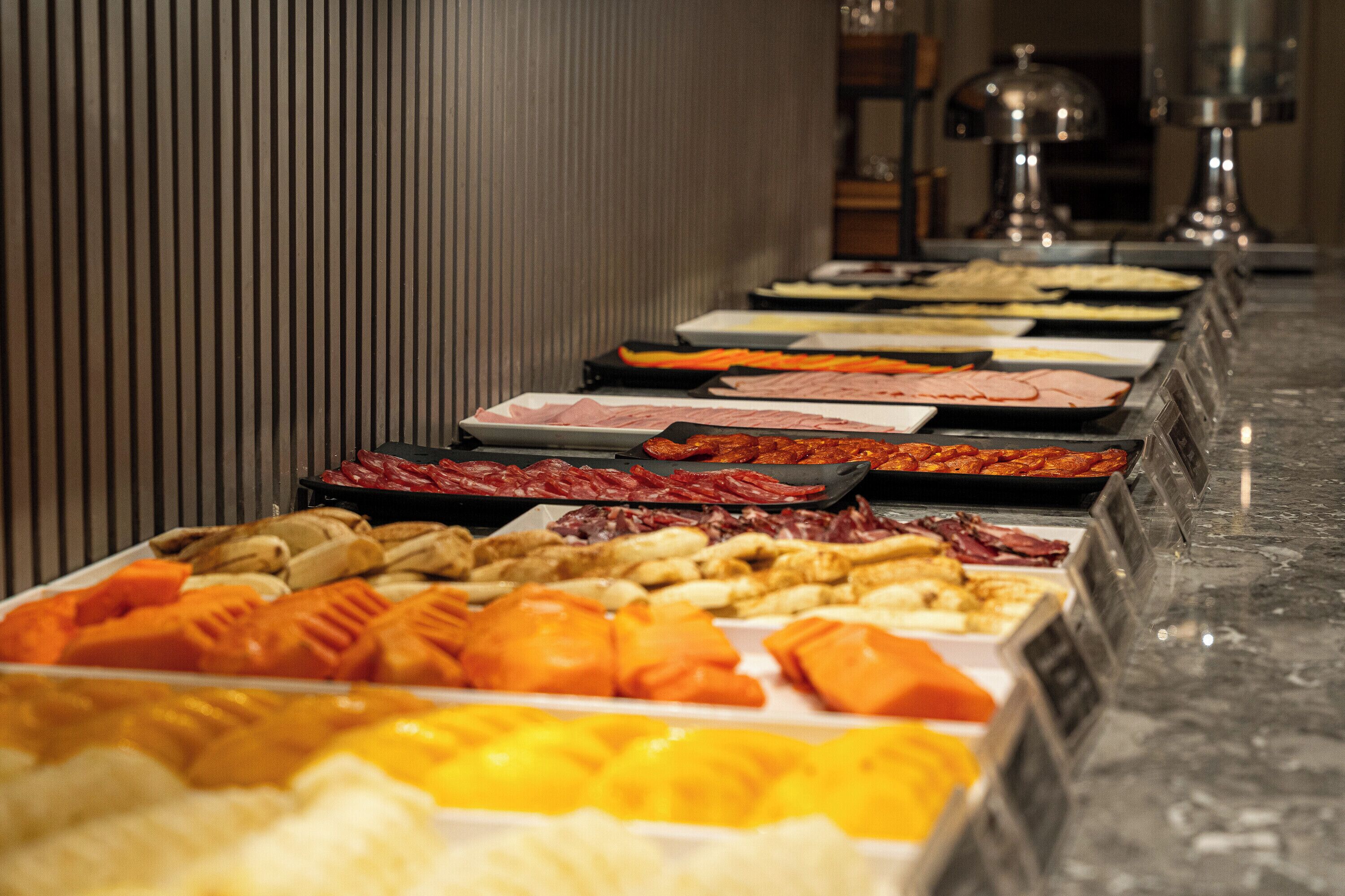 Un bufé con diversas opciones de comida, incluyendo carnes, quesos y frutas.