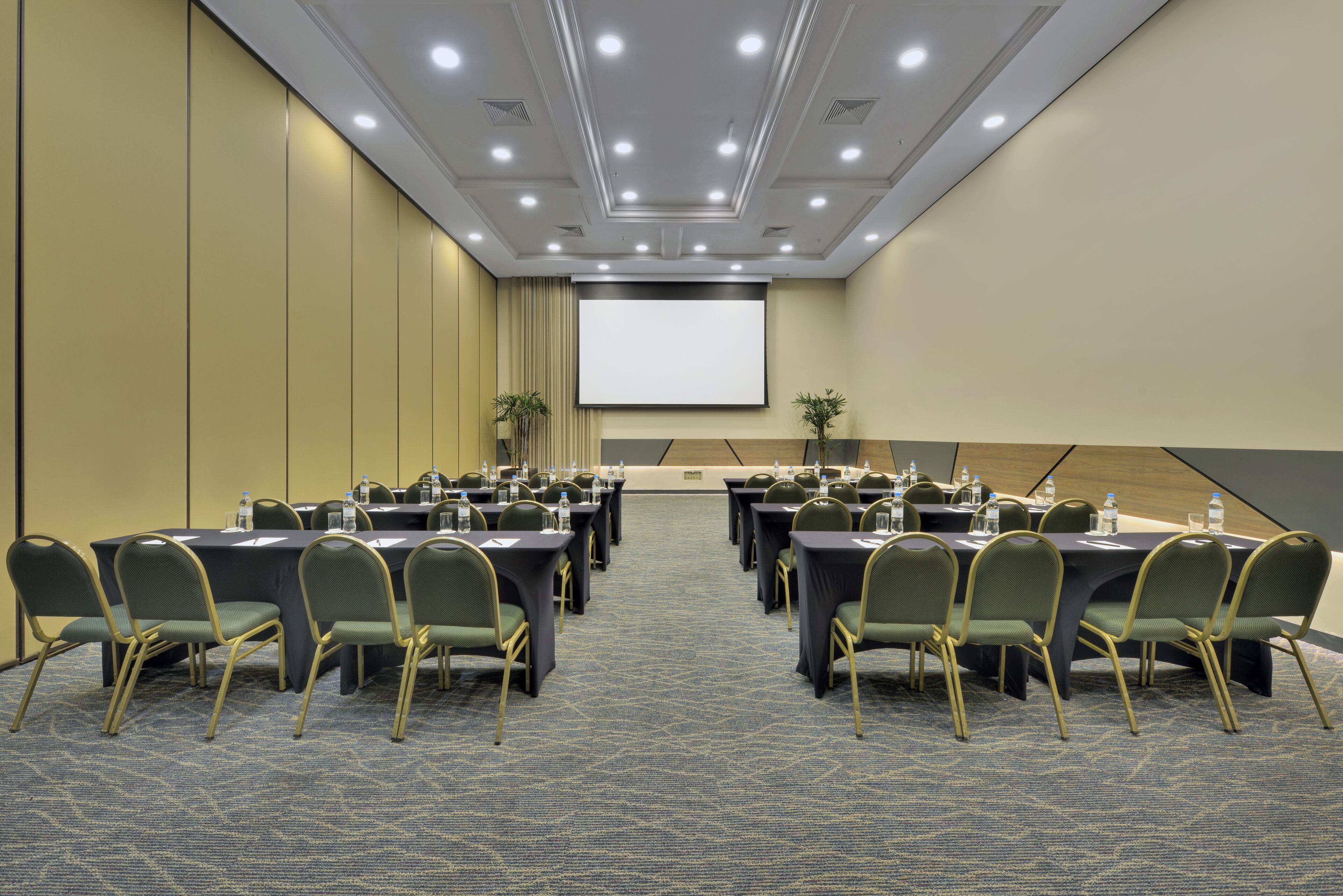 Ein Konferenzraum mit Tischen, Stühlen, einer Projektorleinwand und einem Teppichboden.
