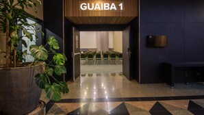 Entrada de un hotel con un letrero que dice "GUAIBA 1", una planta en maceta y una zona de estar con sillas.