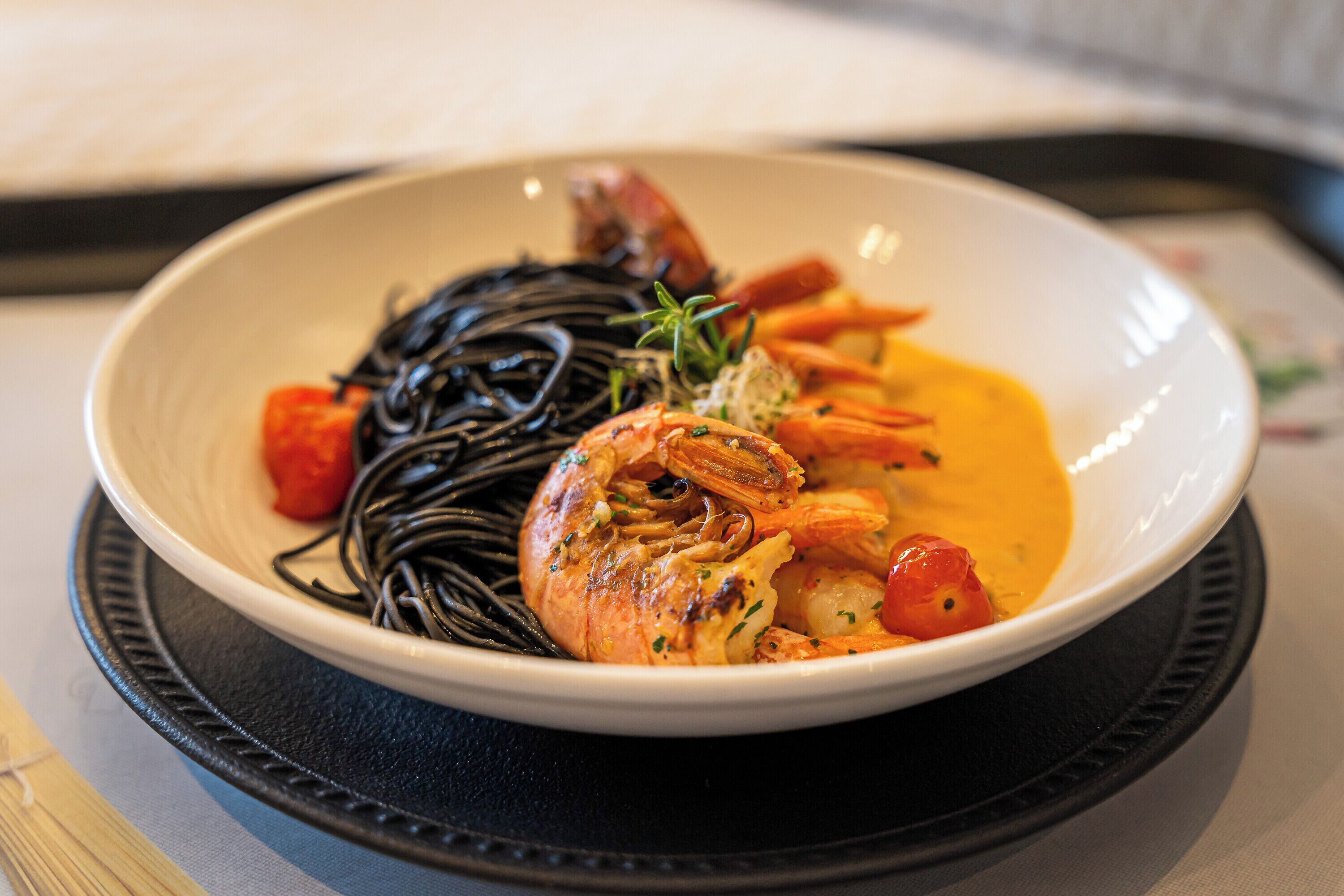 Un bol de nourriture contenant des crevettes, des légumes et des nouilles, le tout servi sur une assiette.