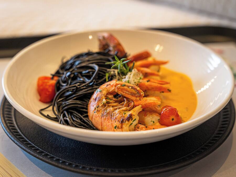 Un bol de nourriture contenant des crevettes, des légumes et des nouilles, le tout servi sur une assiette.