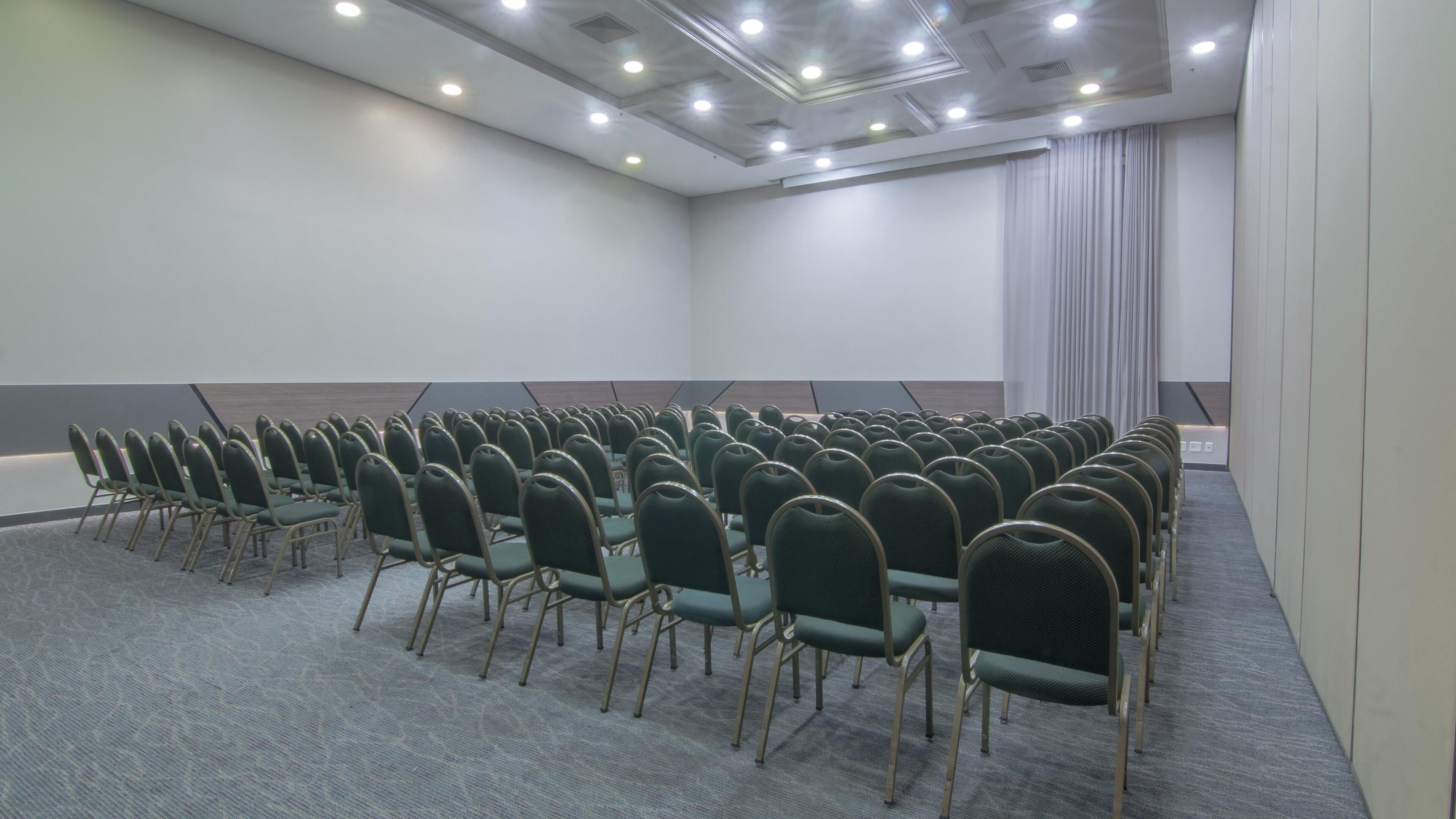 A conference room with rows of green chairs and a carpeted floor.