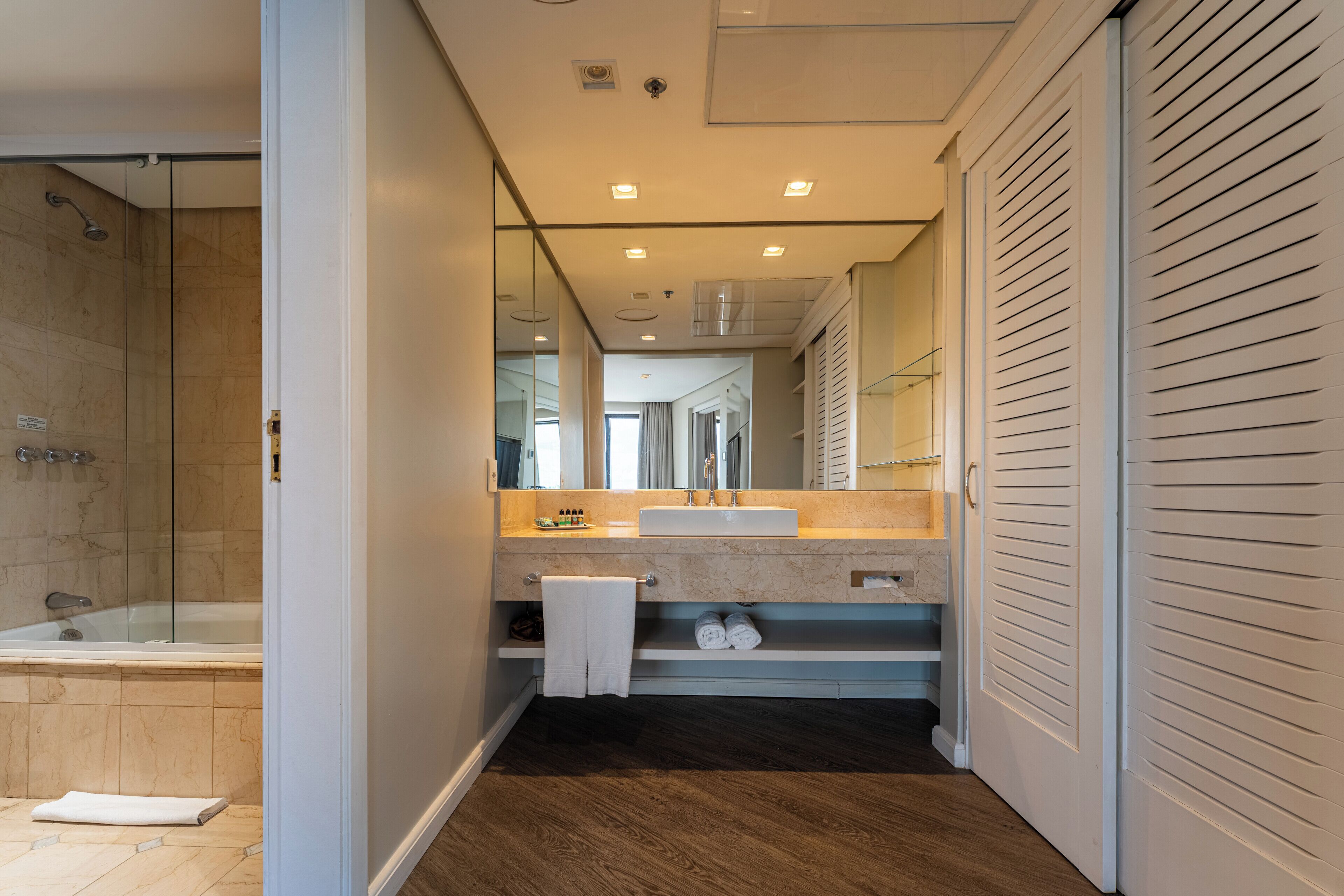 Un baño moderno con cabina de ducha de vidrio, tocador con lavabo y vestidor con puertas correderas.