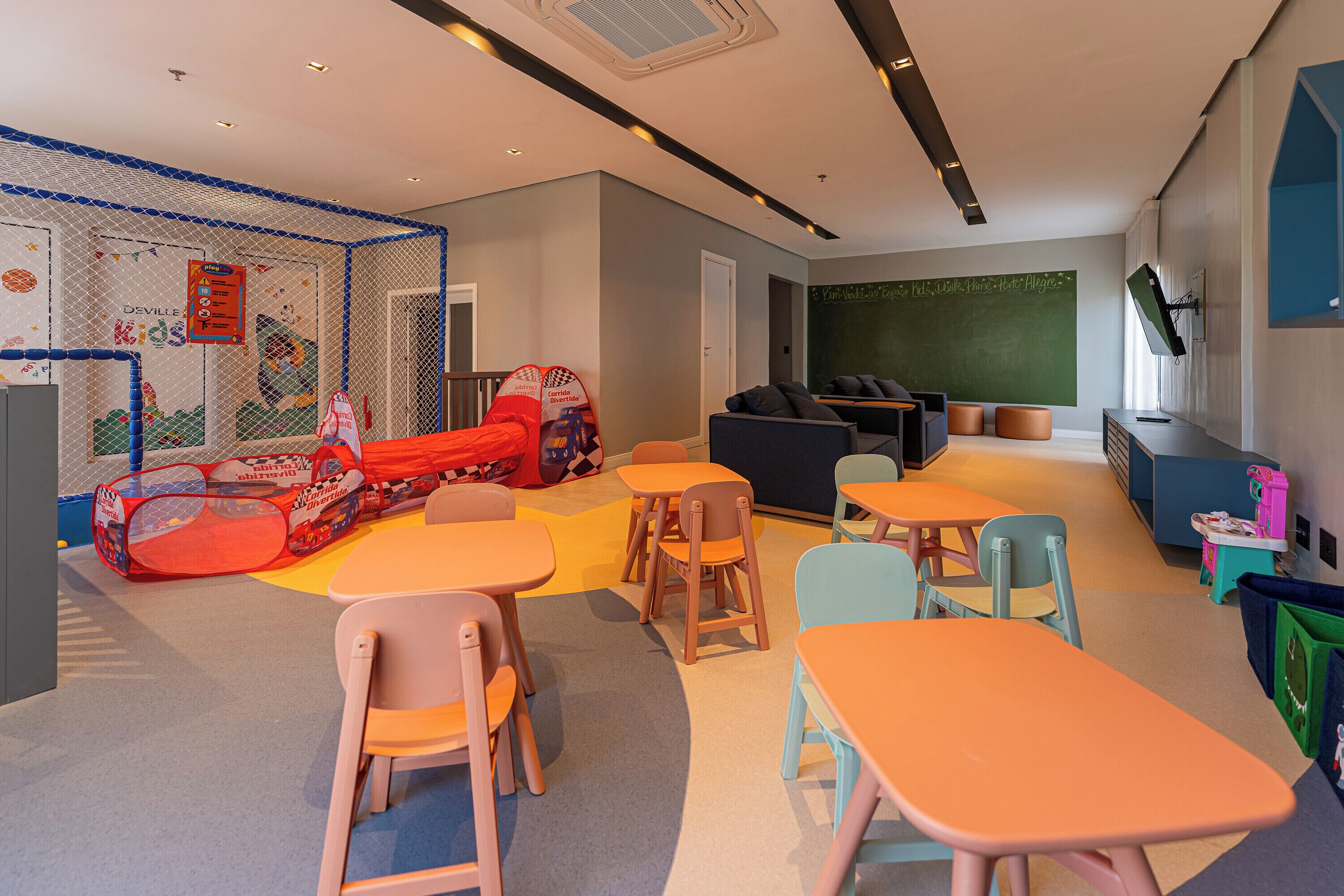 Ein Kinderspielbereich mit einer Kletterwand, bunten Spielgeräten und Sitzgelegenheiten.