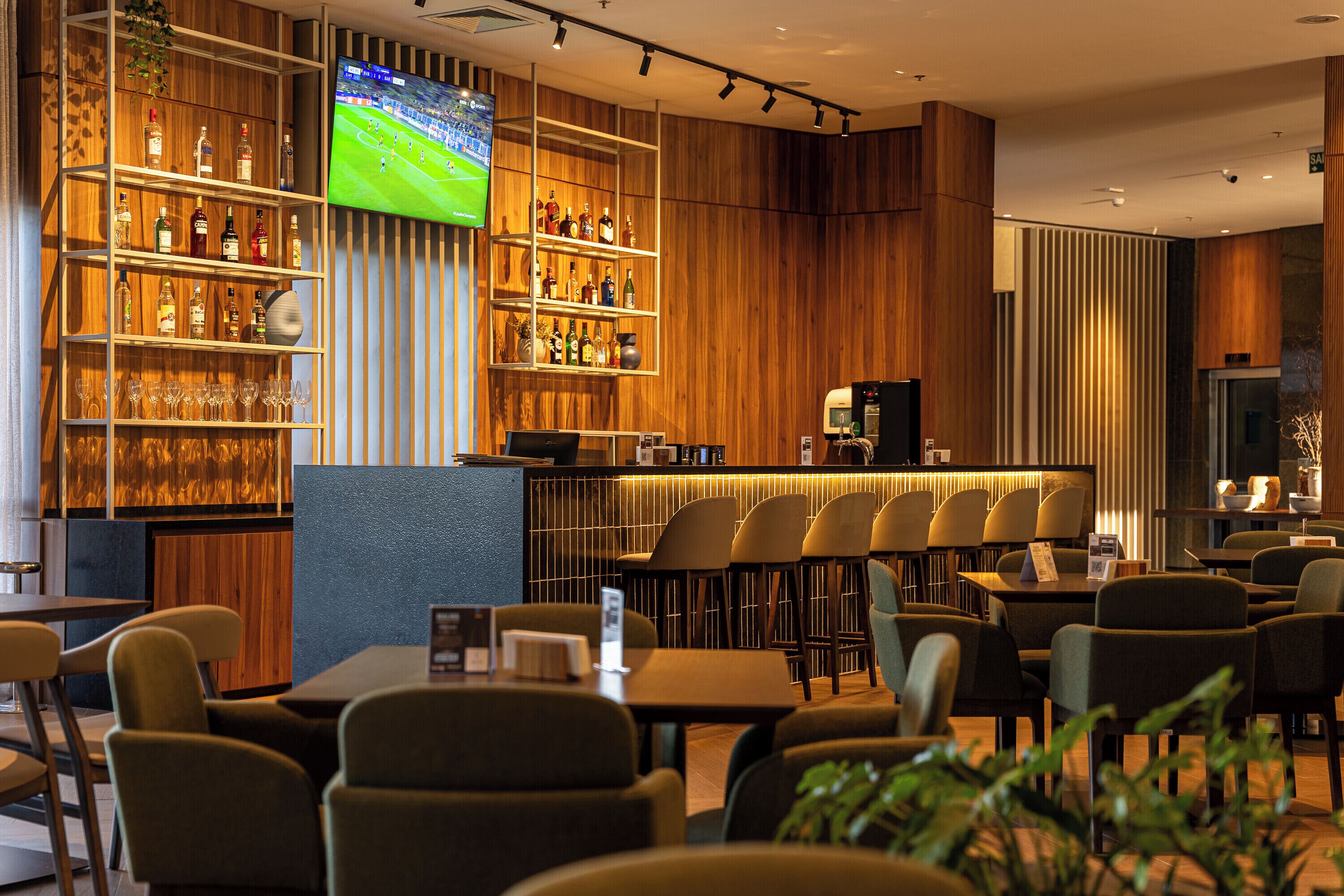 A bar area with shelves of bottles, a television screen, and seating for patrons.