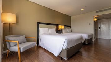 Quarto de hotel com cama, abajures, uma cadeira e uma porta.
