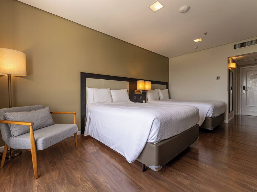 Ein Hotelzimmer mit einem Bett, Nachttischlampen, einem Sessel und einer Tür.