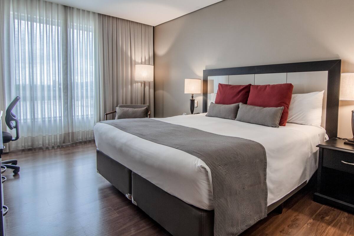 Een hotelkamer met een groot bed, twee nachtkastjes met lampen, een stoel en een bureau met een stoel.