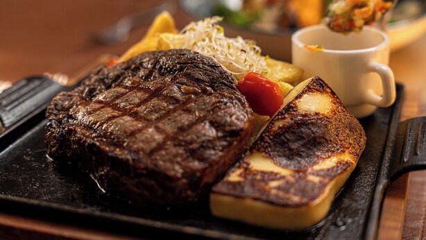 Un bife con marcas de parrilla, una papa a la plancha y una guarnición de verduras en un plato.