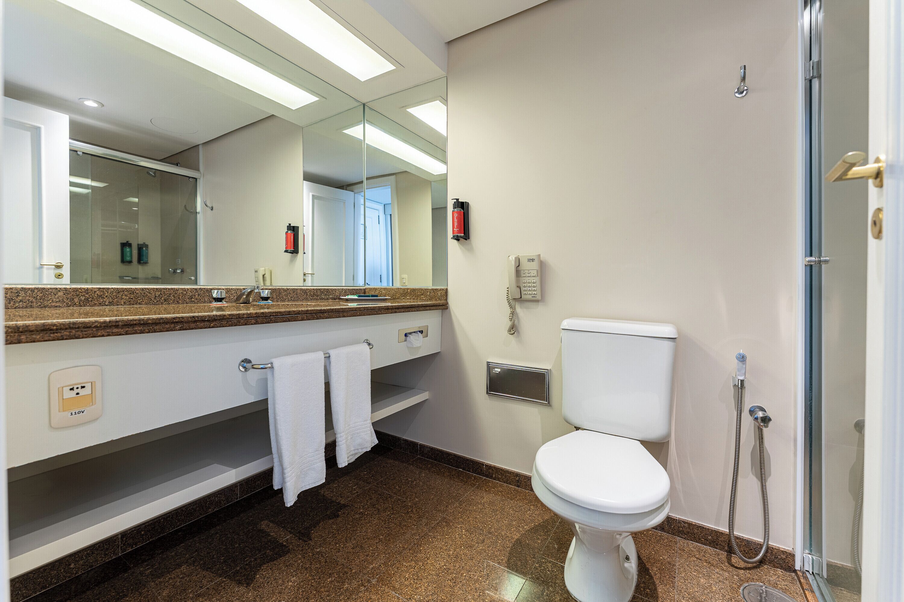 A bathroom with a toilet, a sink with a mirror, a towel rack, and a shower area.