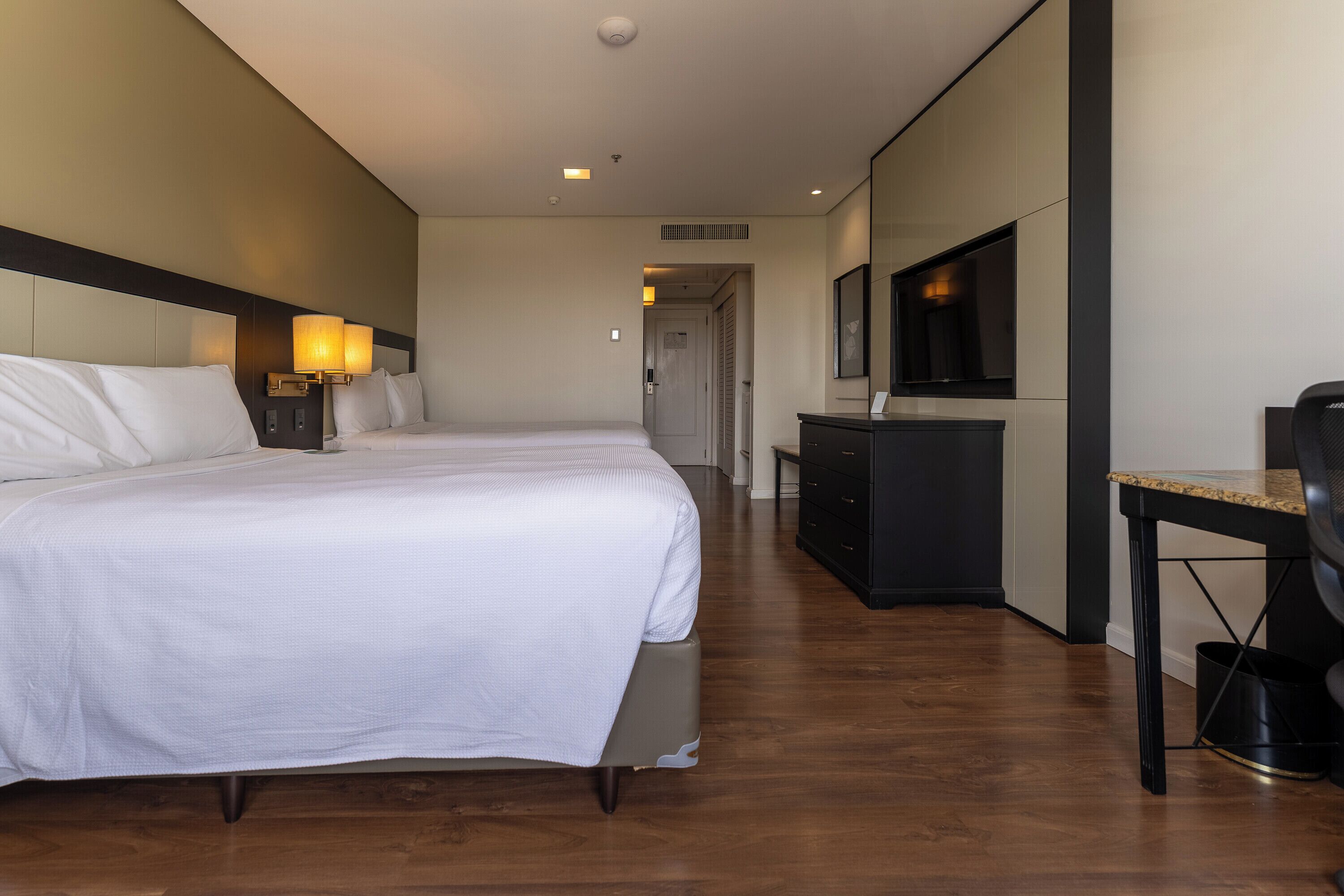 A hotel room with two beds, a desk, a chair, a TV, and a wardrobe.
