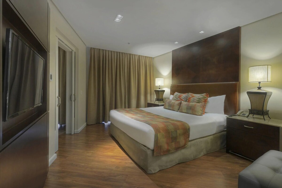 Une chambre d’hôtel avec un grand lit, deux tables de chevet avec des lampes, une armoire et un grand miroir.