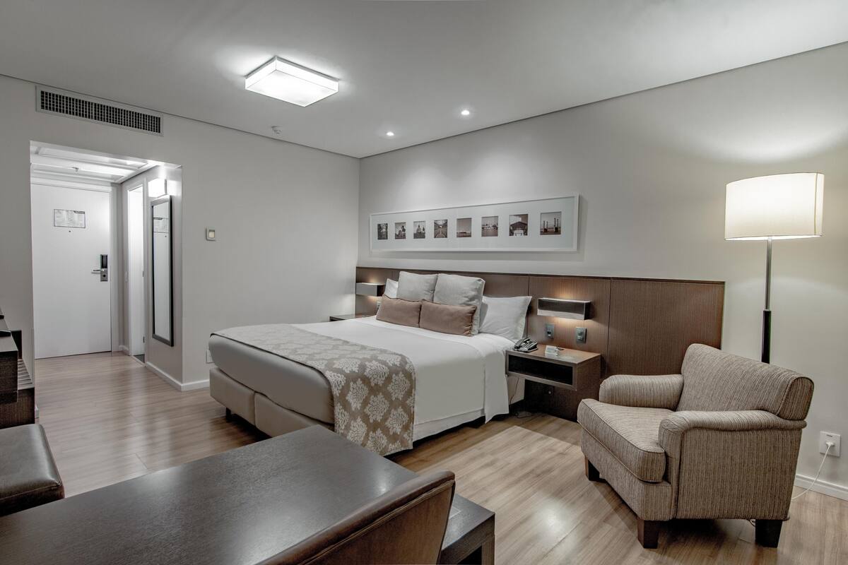 Een moderne hotelkamer met een groot bed, nachtkastjes, een stoel en een bureau.