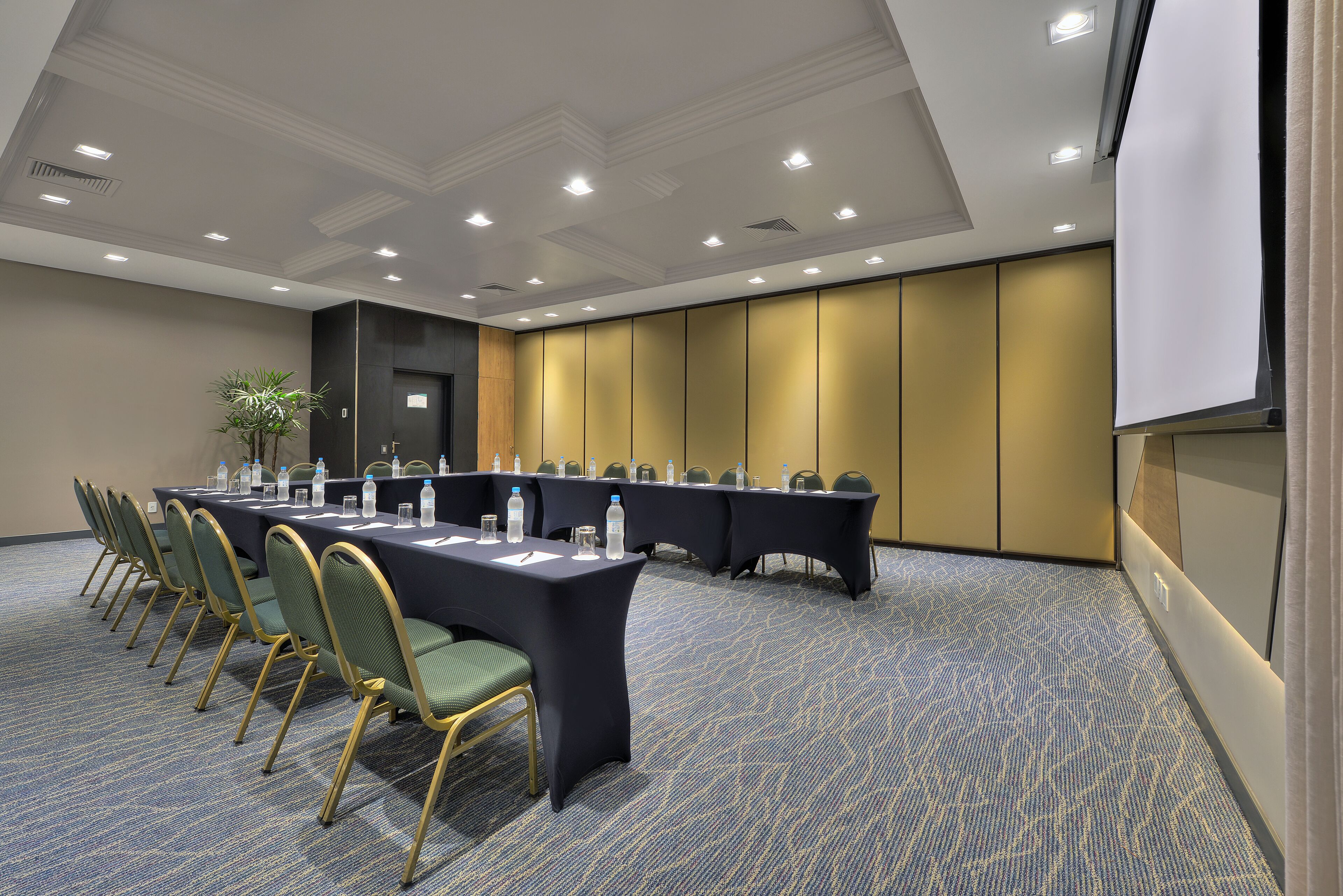 Uma sala de conferências com uma mesa comprida, cadeiras e uma tela de projetor.