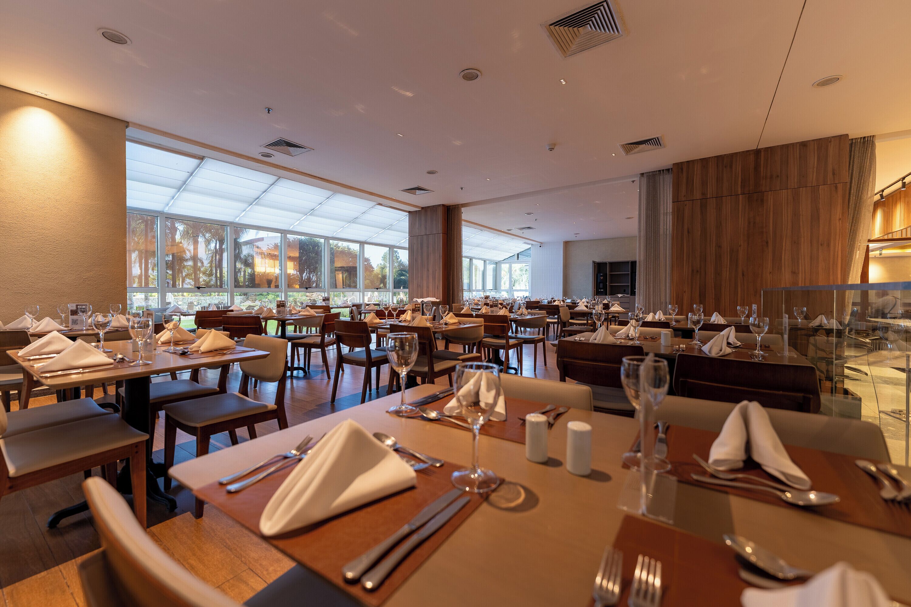 Un restaurante espacioso con varias mesas, sillas y un amplio ventanal con vistas al exterior.