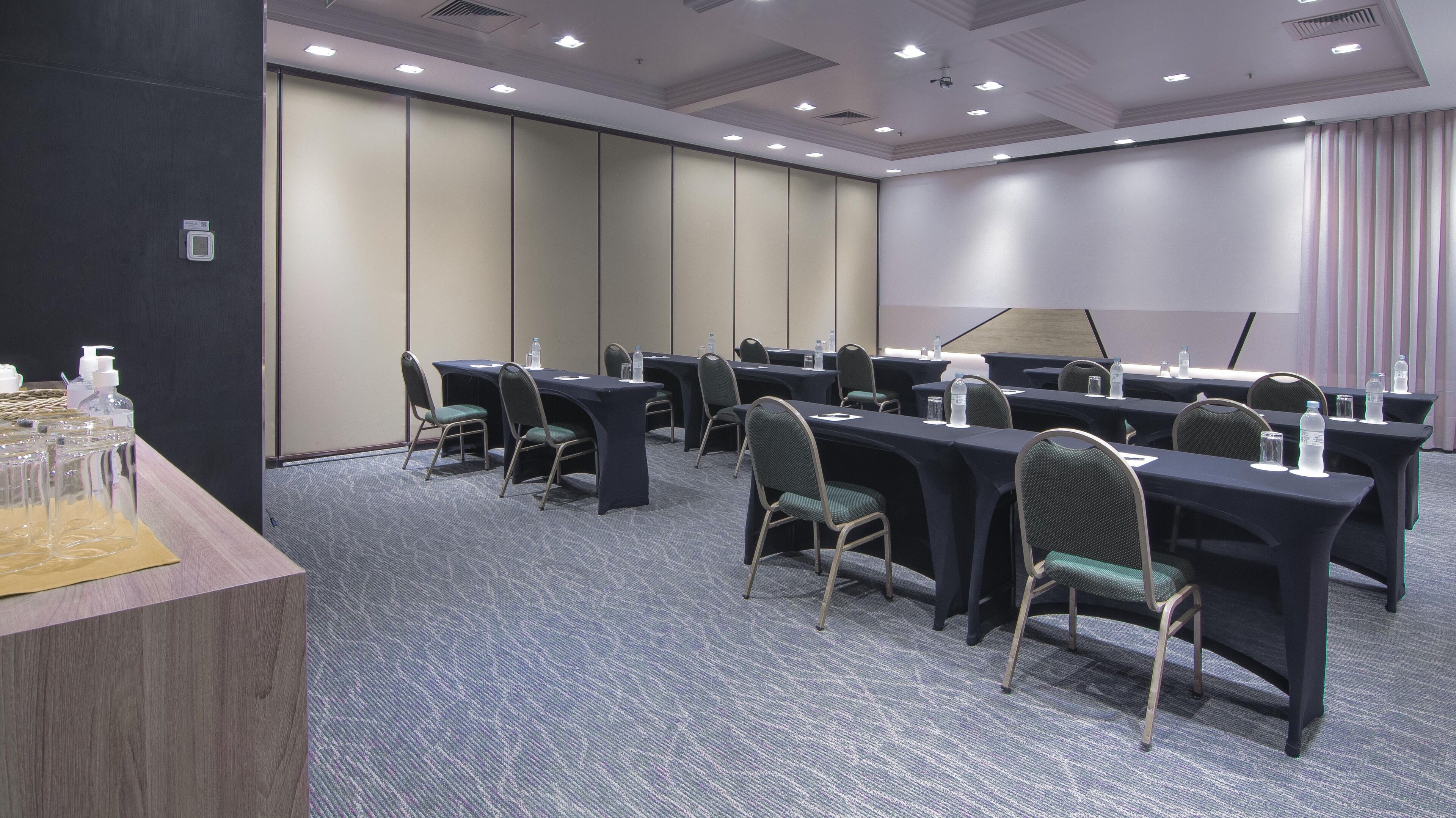 Un salón de conferencias con varias mesas y sillas, equipado con botellas de agua y tarjetas de identificación.