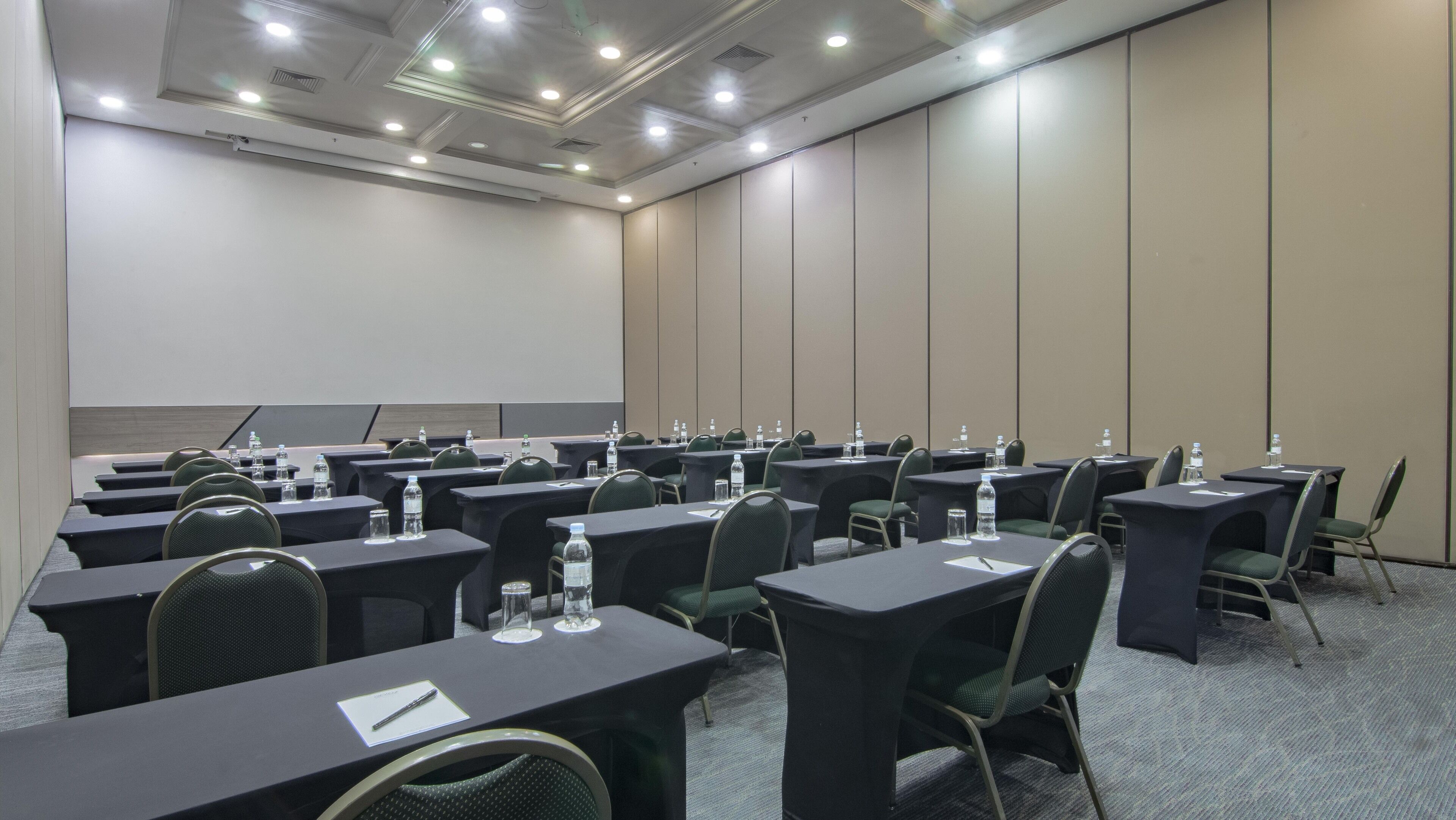 A conference room with multiple tables and chairs, equipped with water bottles and notepads.