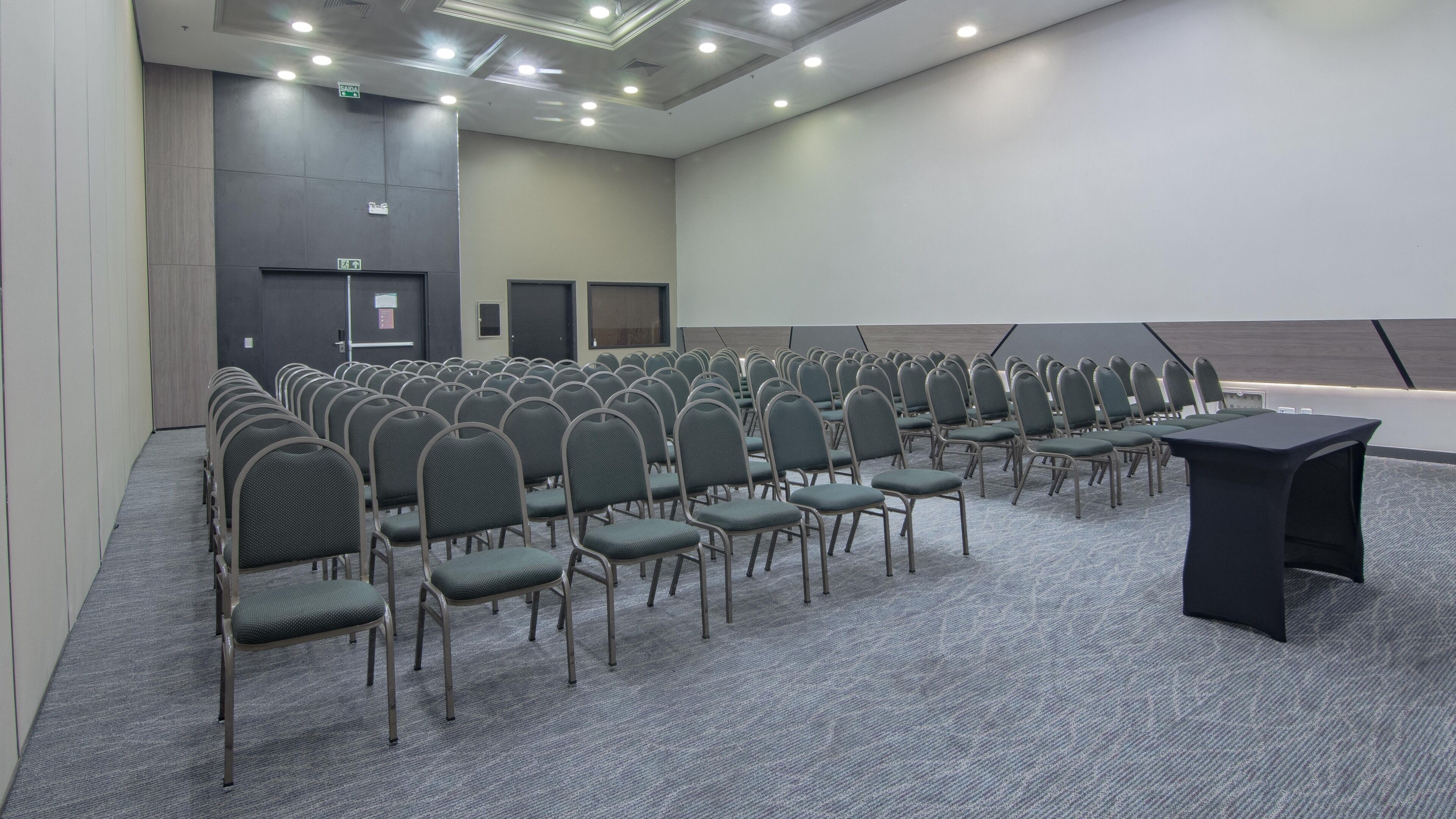 Una sala conferenze con file di sedie, uno schermo per proiezioni e un podio.