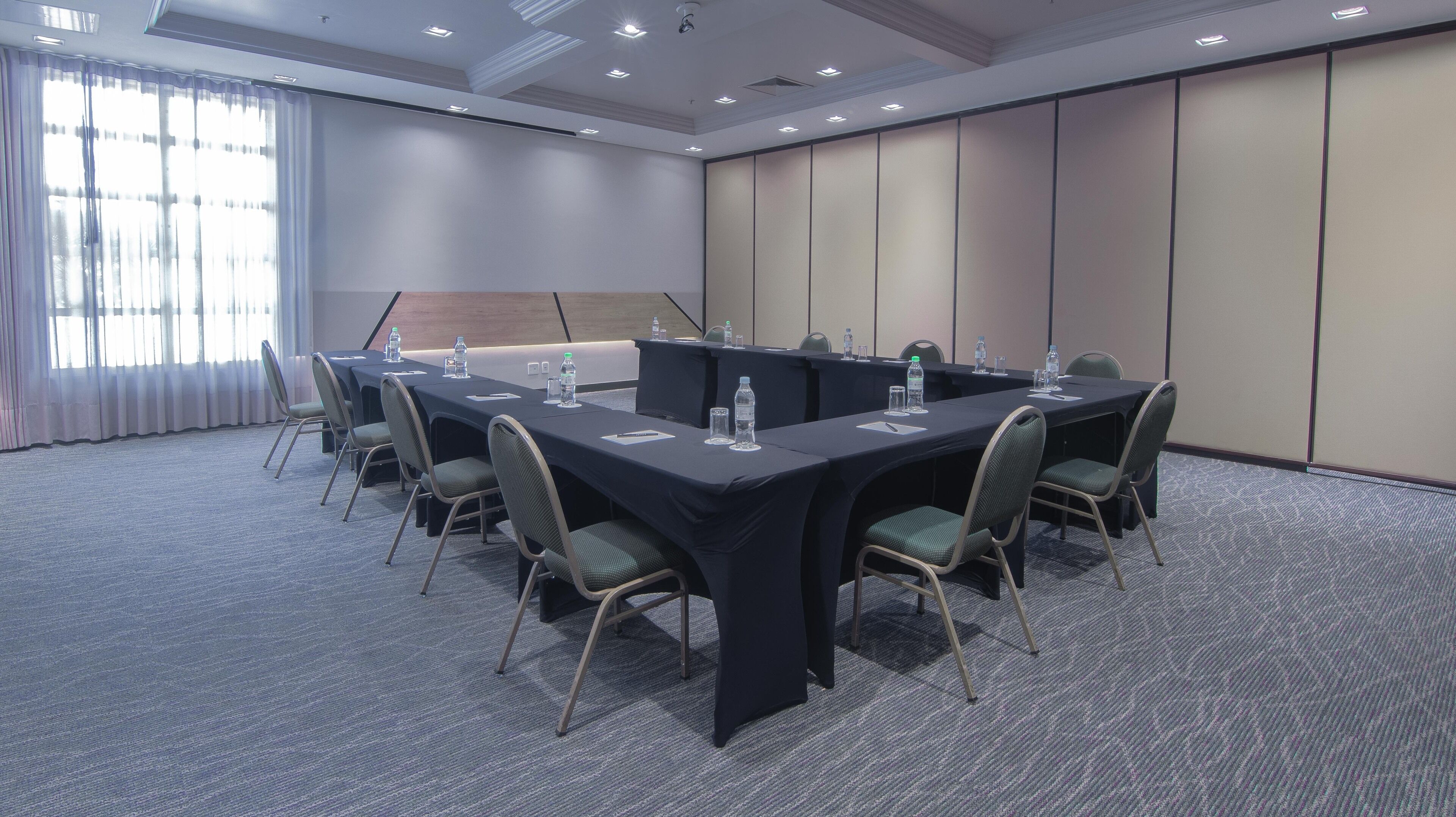 Un salón de conferencias con una larga mesa, sillas y botellas de agua.