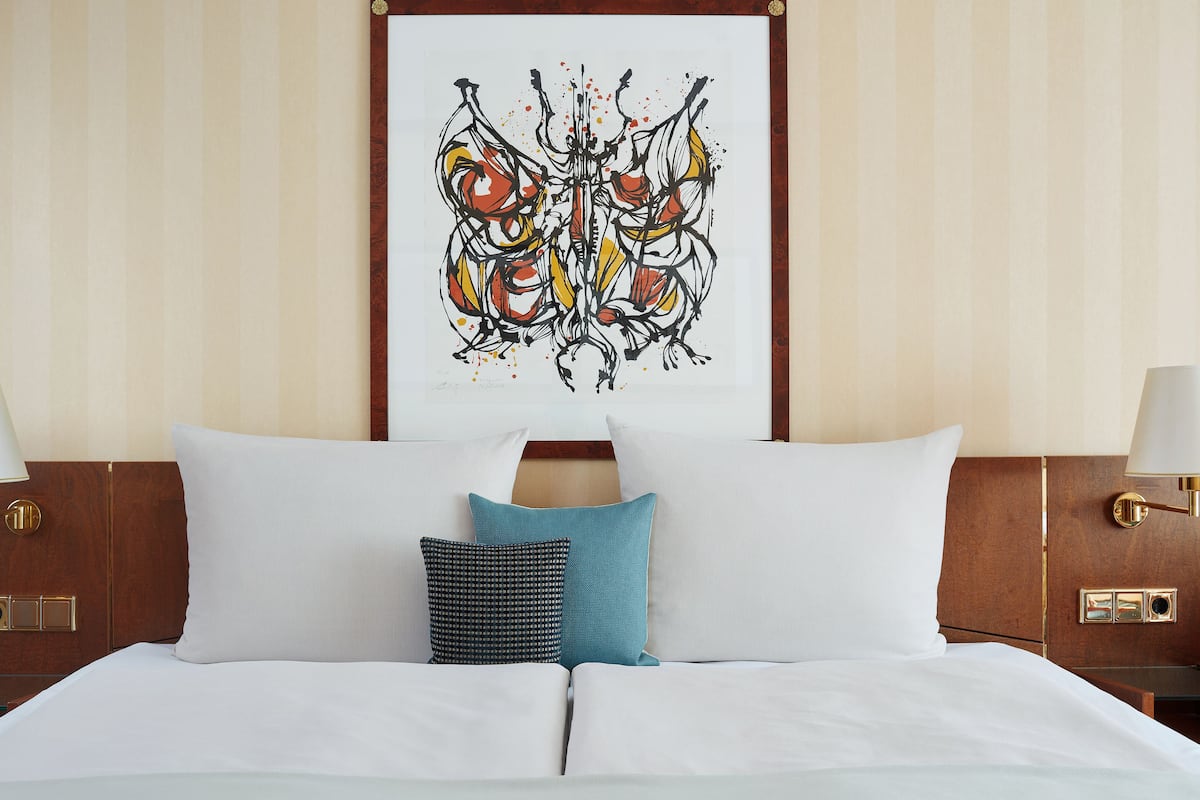 Habitación de hotel con una cama grande, dos lámparas de noche y un cuadro abstracto enmarcado en la pared.
